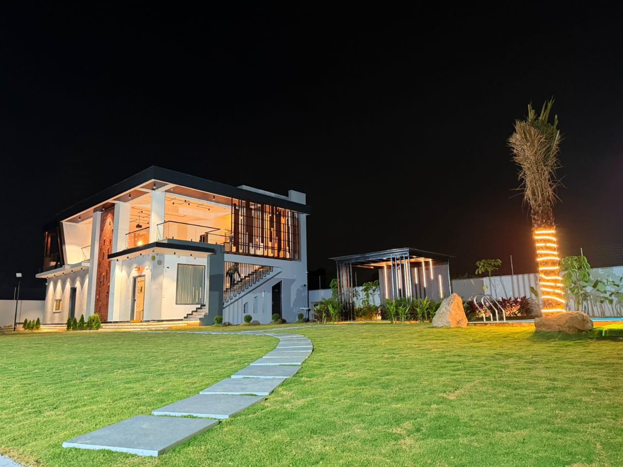 D Treatfarms villa exterior glowing at dusk — private farmhouse Pocharam Hyderabad